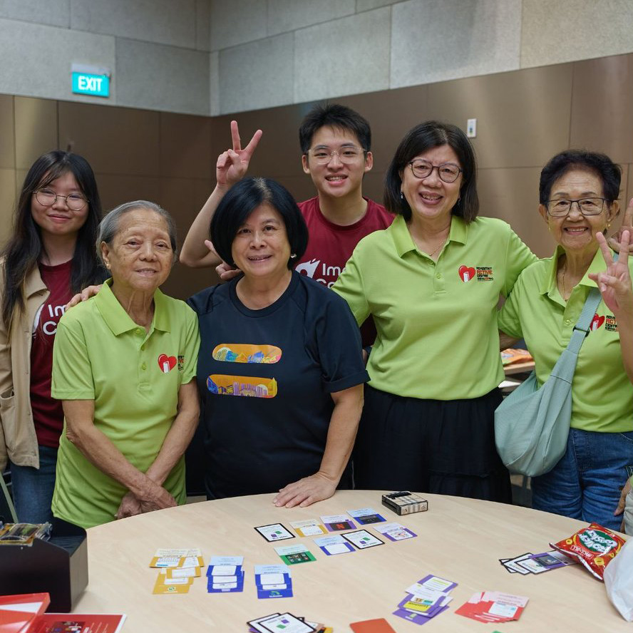 Youth volunteers with seniors from Adventist Active Centre, gathered around The Archive's card game